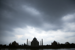 Silhouette of the Taj Mahal under storm clouds as seen from Mehtob Bagh Park across the Yamuna River in Agra, India.