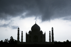 Silhouette of the Taj Mahal under storm clouds as seen from Mehtob Bagh Park across the Yamuna River in Agra, India.
