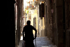 An elderly woman is walks down a narrow cobblestone street in Naples, Italy.