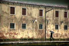 A man carrying and umbrella walks along a terra-cotta building in Venice, Italy