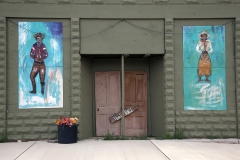 Murals depicting a cowboy and cowgirl on a wall of a rundown building in Elida, New Mexico.